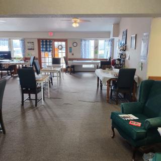 A spacious indoor living and dining area with chairs, tables, and carpeted flooring.