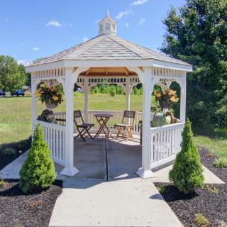 A charming white gazebo with outdoor seating surrounded by greenery and plants in a garden setting.