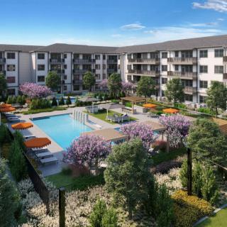 A modern residential complex featuring a central swimming pool surrounded by lush landscaping and outdoor seating.