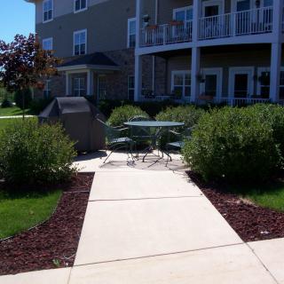 A sunny patio area with outdoor furniture and lush greenery in front of a residential building.