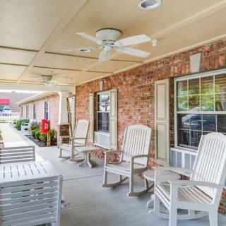 A cozy porch with white rocking chairs and a ceiling fan attached to a brick building.
