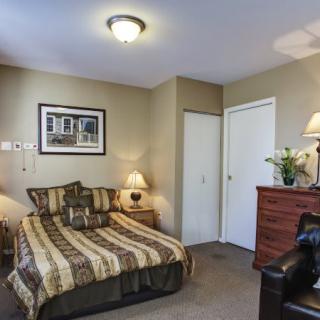 A cozy bedroom with a neatly made bed, bedside lamp, dresser, and decorative elements.
