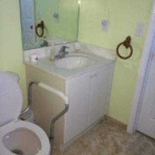 A small bathroom with a sink, toilet, and mirror, featuring green-painted walls and tiled flooring.