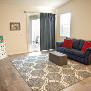 A cozy living room with a blue sofa and red pillows, featuring a patterned rug and dark curtains.