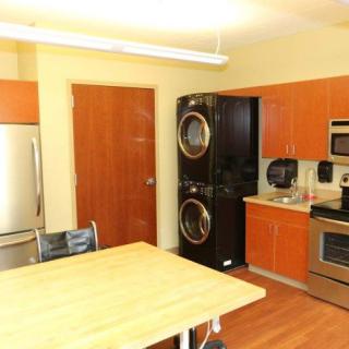 A modern kitchen featuring a stainless steel stove, microwave, and refrigerator, along with a stacked washer and dryer unit and a wooden table.