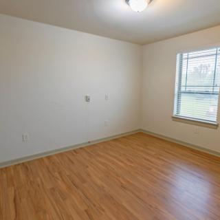 An empty room with hardwood flooring, a window, and a ceiling light fixture.