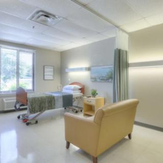 A clean and modern hospital room with a bed and seating area.