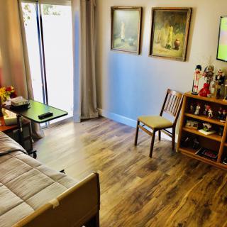 A cozy living room with wooden flooring, decorated with paintings and simple furniture.
