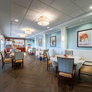 A well-decorated dining area with neatly arranged tables and chairs, featuring elegant lighting and artwork on the walls.