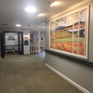A well-lit hallway with a large framed painting on the wall and a carpeted floor.