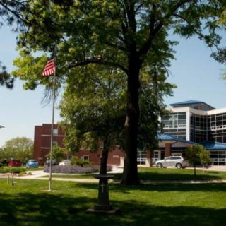 A scenic view of a modern building surrounded by trees and a flagpole on a sunny day.