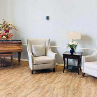 A cozy living room with two armchairs, a side table with a lamp, and a piano adorned with flowers.