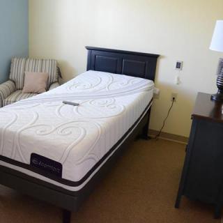 A bedroom with a single bed and mattress, alongside furniture and a lamp.