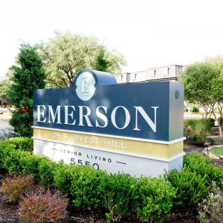 The image shows an outdoor sign for Emerson, surrounded by greenery.