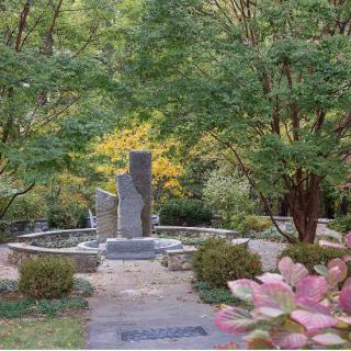 A tranquil garden with a stone monument surrounded by lush greenery and a winding pathway.