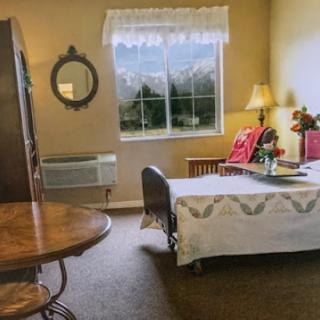 A cozy and well-lit bedroom featuring a neatly made bed, a round table, and a large window offering a glimpse of the outside.