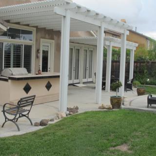 A backyard patio with a white pergola and outdoor kitchen setup.