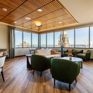 A modern lounge area with comfortable seating, large windows offering a city view, and warm wood design elements.
