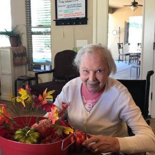 An elderly woman in a wheelchair enjoys crafting with autumn leaves indoors.