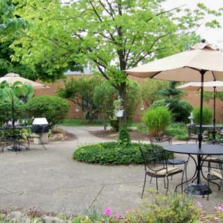 A serene garden patio with tables, chairs, and umbrellas surrounded by lush greenery.