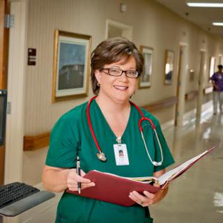A nurse in scrubs holding a patient chart, smiling as she walks through the hospital corridor.