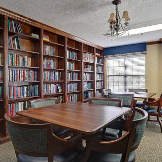 A cozy library room with bookshelves and a wooden table surrounded by chairs.