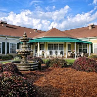A scenic view of a building with a fountain and landscaped garden under a partly cloudy sky.