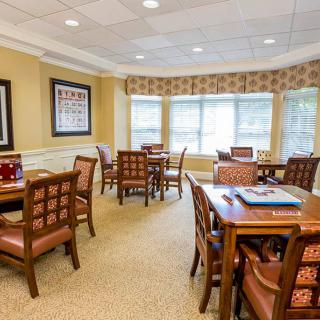 A well-lit dining area with several tables and chairs, featuring large windows and a carpeted floor.