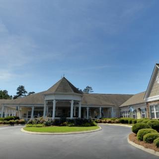 A large, elegant building with a circular driveway and neatly landscaped grounds under a clear sky.