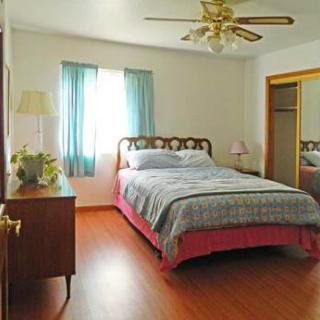 A cozy bedroom with a bed, ceiling fan, and a window with curtains.