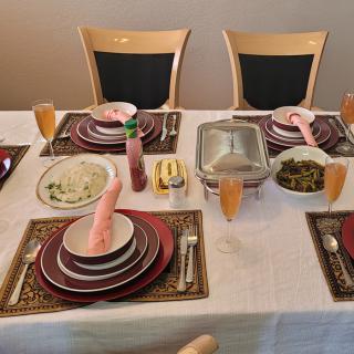 A well-arranged dining table set for a meal, featuring plates, cutlery, glasses, and pink folded napkins on a white tablecloth.