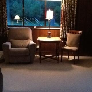 A cozy living room with a lamp, chair, and table near a window.