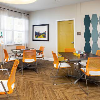 A modern dining area with orange chairs and glass tables, featuring contemporary decor and bright accents.