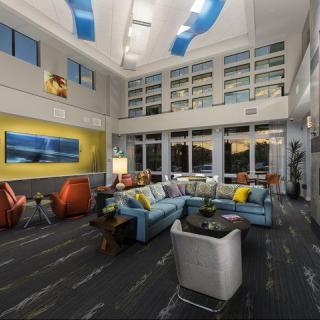 A modern living room with high ceilings, featuring comfortable seating and large windows.