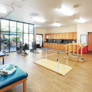 A well-equipped rehabilitation room with exercise equipment and parallel bars for physical therapy.