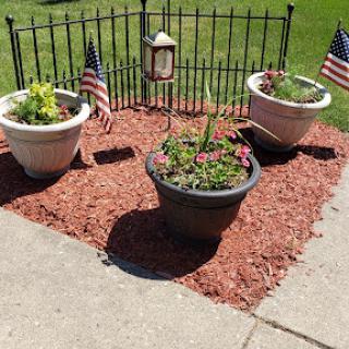 A charming garden area featuring flower planters adorned with small American flags and surrounded by decorative red mulch.