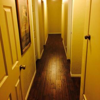 A dimly lit hallway with yellow walls and multiple doors on each side, featuring a wooden floor.