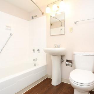A minimalist bathroom featuring a bathtub, pedestal sink, and toilet with white walls.