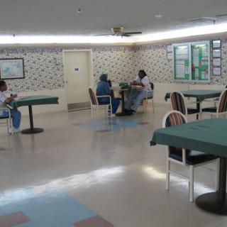 A view of a recreation room with tables and chairs, where a few individuals are engaged in activities.