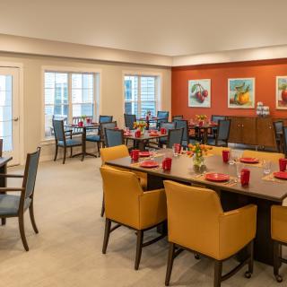 A well-decorated dining area featuring tables with red dishware, surrounded by comfortable chairs and adorned with colorful art on an orange accent wall.