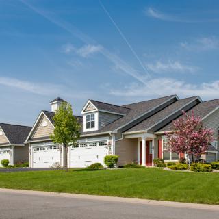 A row of suburban houses with well-maintained lawns and driveways under a clear blue sky.