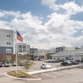 A modern building complex with an adjacent parking lot and an American flag flying under a partly cloudy sky.