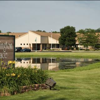 A building complex with a sign and pond in the foreground, surrounded by a well-maintained lawn and trees.