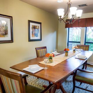 A well-lit dining room with a wooden table and chairs, decorated with artwork and flowers.