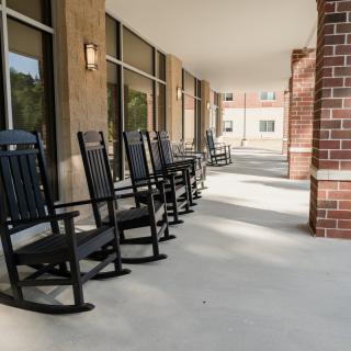 A row of black rocking chairs on a porch with brick and glass walls.