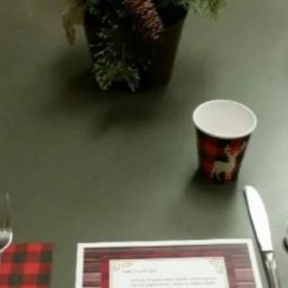 A holiday-themed table setting with a plaid cup, menu, and festive centerpiece.