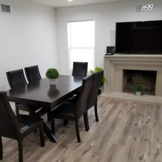 A modern dining room with a sleek table and chairs, featuring a fireplace and a mounted television.