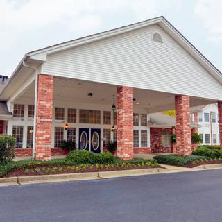 A brick building with an entrance supported by columns and surrounded by landscaping.