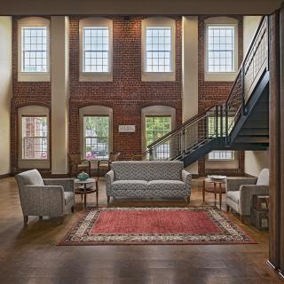 A spacious living room featuring a classic brick wall, multiple large windows, comfortable seating arrangements, and a modern staircase.