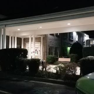 A well-lit entrance of a building at night surrounded by neatly trimmed hedges.